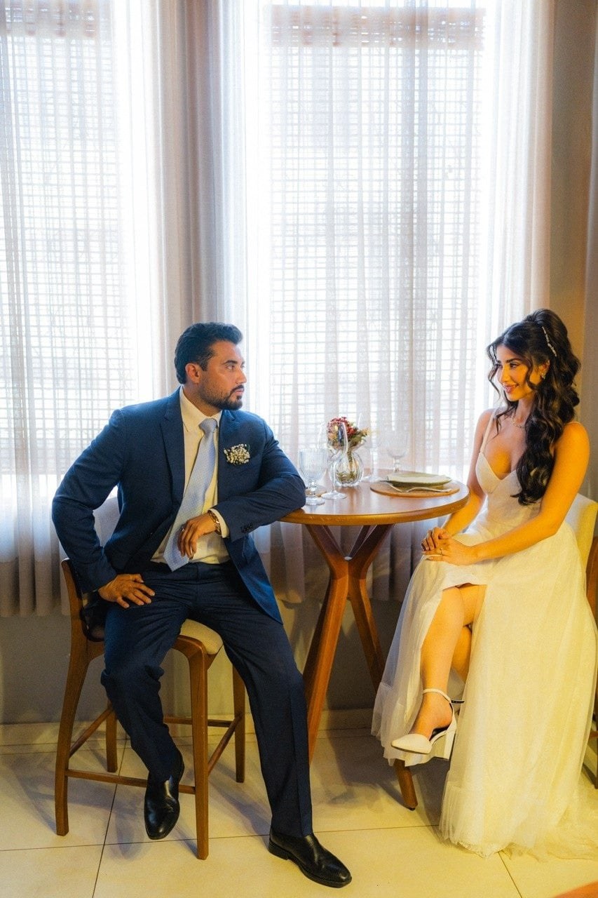 Monique y Luis, sentados frente a frente en una mesa junto a la ventana